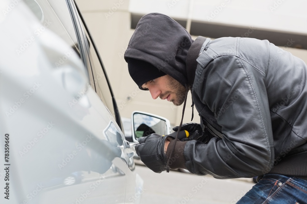 Thief breaking into car with screwdriver Thief breaking into car with screwdriver
