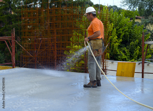 Photography Construction worker watering fresh concrete slab using a hose