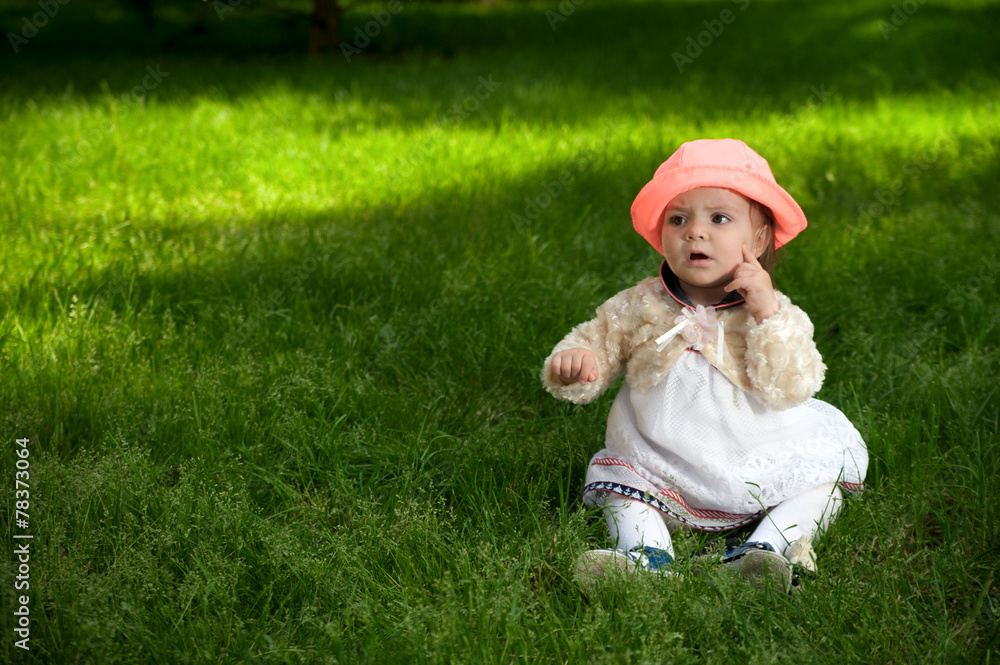 A little baby in bright hat is sitting on the grass A little baby in bright hat is sitting on the grass