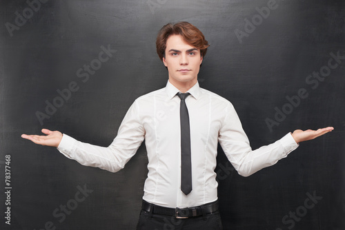 Serious man with palms up on chalkboard background