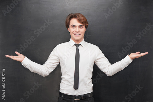 Cheerful man with palms up on chalkboard background