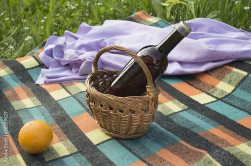 Bottle in basket with orange and shirt on picnic blanket
