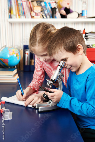 Girl and boy uses a microscope and writes results