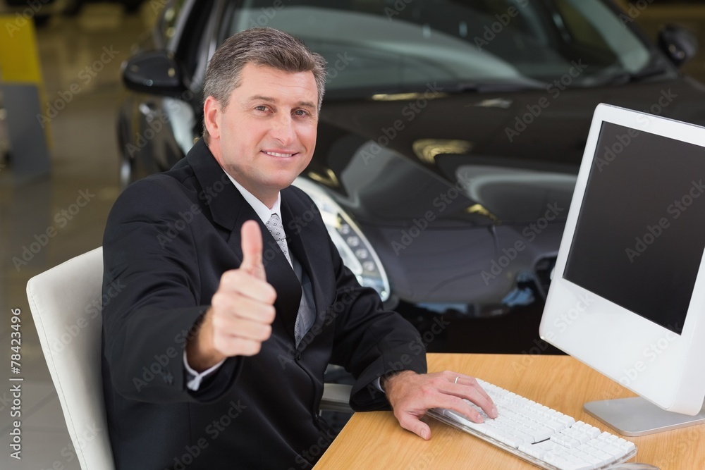 Smiling businessman giving thumbs up at his desk Smiling businessman giving thumbs up at his desk