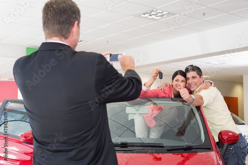 Businessman taking picture of the couple in their new car