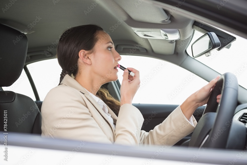 Businesswoman using mirror to put on lipstick while driving Businesswoman using mirror to put on lipstick while driving