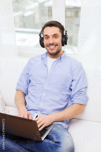 smiling man with laptop and headphones at home