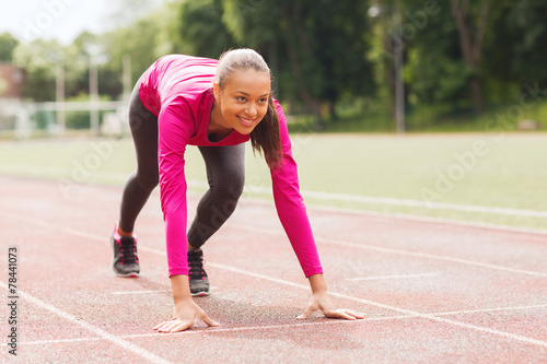 smiling young woman running on track outdoors