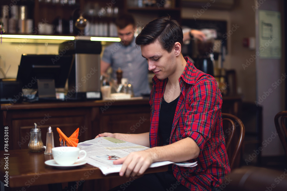 Young attractive student drinking coffee and reading newspaper