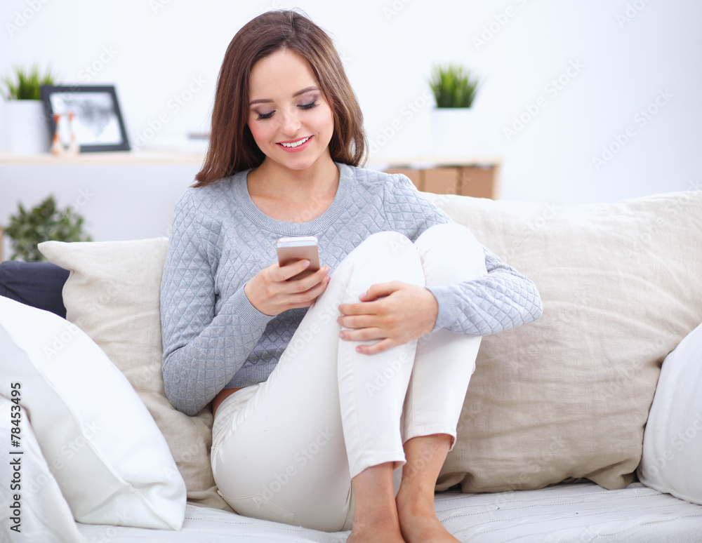 Pretty girl using her smartphone on couch at home in the living Pretty girl using her smartphone on couch at home in the living