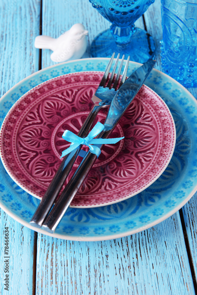 Empty colorful plate, glasses and silverware set on wooden Empty colorful plate, glasses and silverware set on wooden