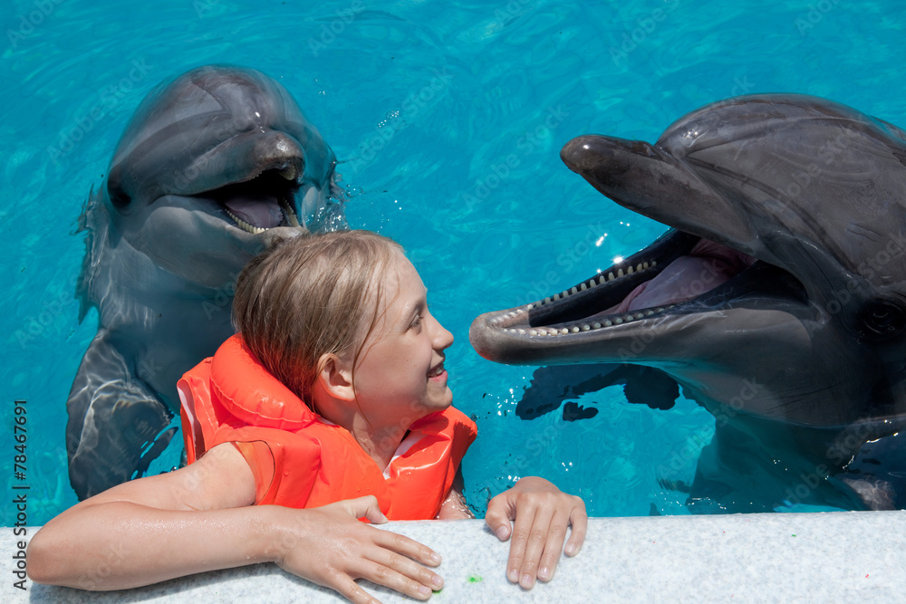 Obraz premium Szczęśliwa dziewczynka śmiejąc się z dwoma delfinami w basenie