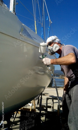 man with face mask spray painting sail boat yacht with air gun