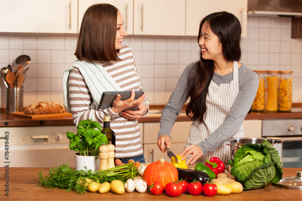 Two smiling female friends are cooking together at home
