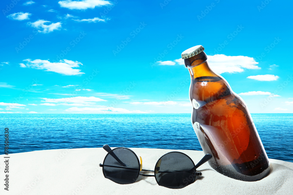 Obraz premium Bottle beer and sunglasses in the sand of a tropical beach