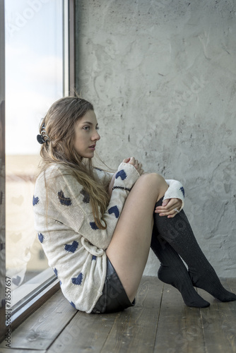 Beautiful  girl sitting at a window in a warm sweater and socks