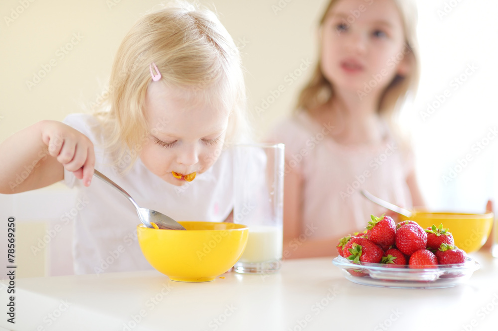 Two cute little sisters eating cereal in a kitchen Two cute little sisters eating cereal in a kitchen