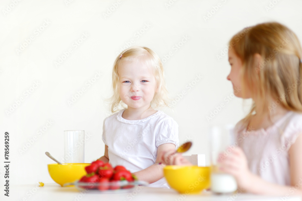 Two cute little sisters eating cereal in a kitchen