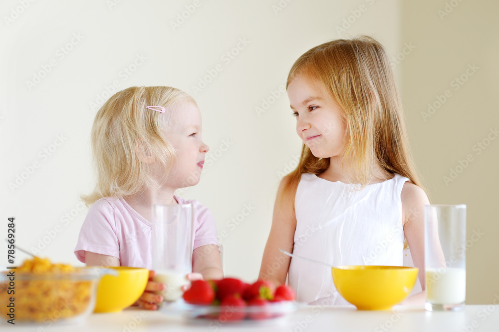 Two cute little sisters eating cereal in a kitchen Two cute little sisters eating cereal in a kitchen