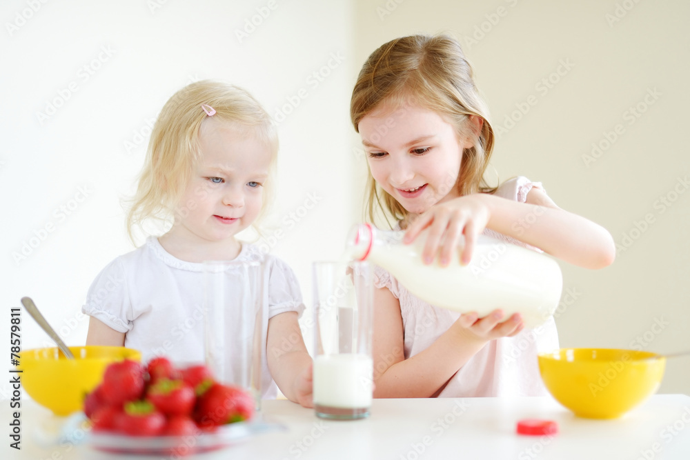 Two cute little sisters eating cereal in a kitchen Two cute little sisters eating cereal in a kitchen