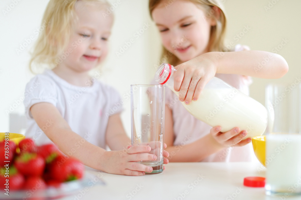 Two cute little sisters eating cereal in a kitchen Two cute little sisters eating cereal in a kitchen