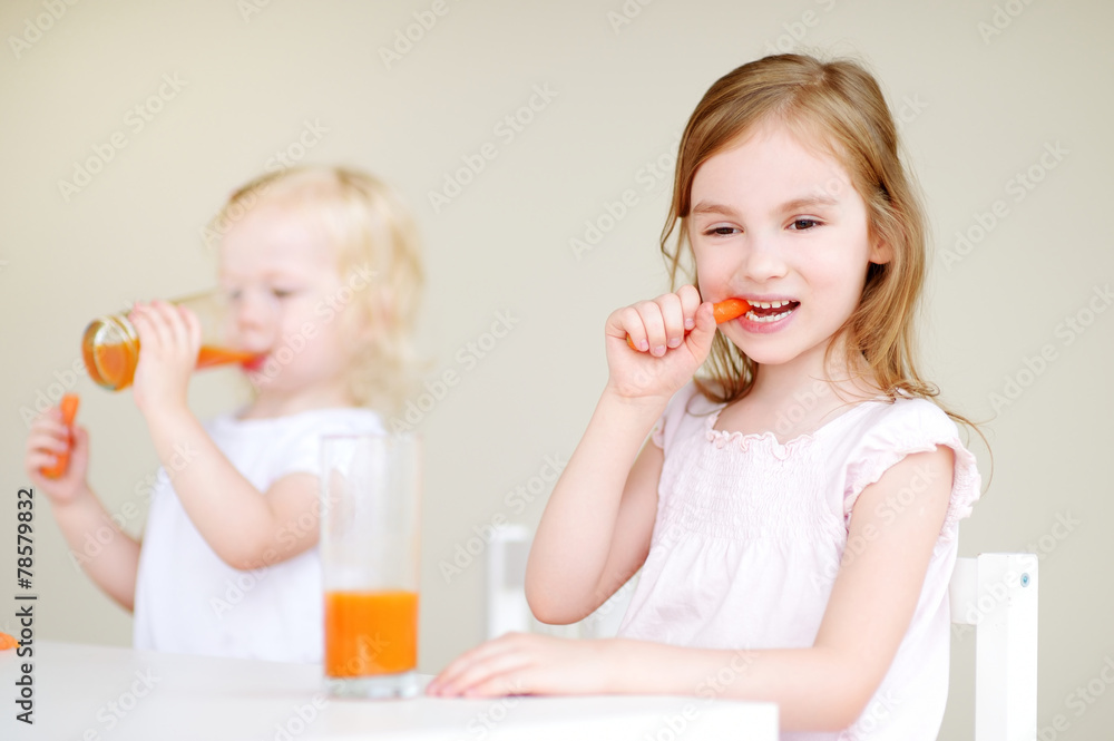 Two cute little sisters drinking carrot juice Two cute little sisters drinking carrot juice