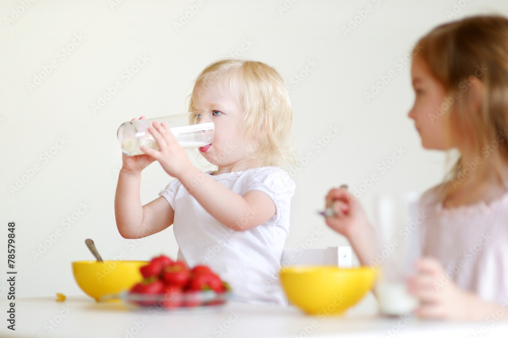 Two cute little sisters eating cereal in a kitchen Two cute little sisters eating cereal in a kitchen
