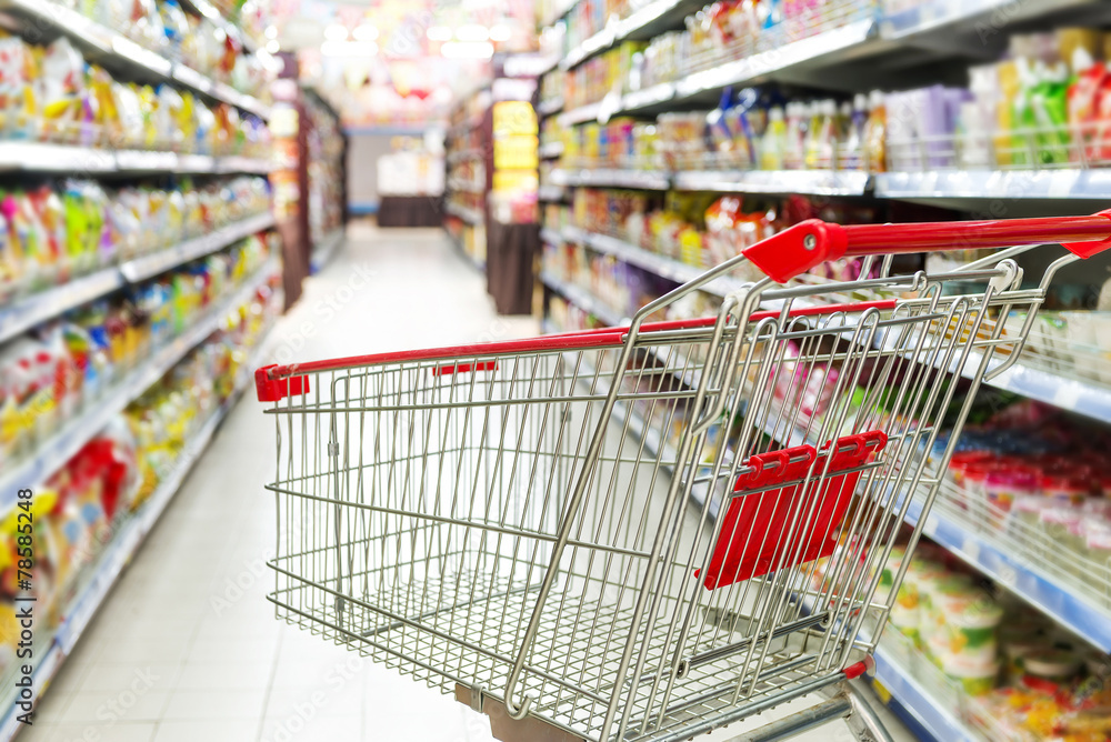 Supermarket interior, empty red shopping cart.