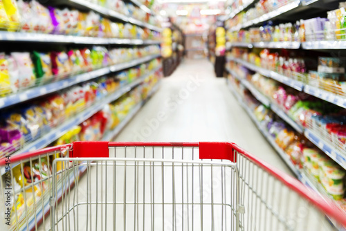 Supermarket interior, empty red shopping cart.