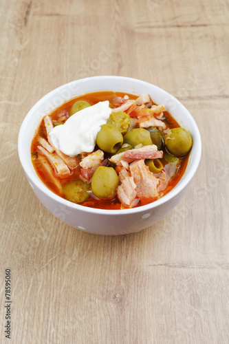 Soup saltwort with lemon, meat, pickles, tomato sauce olives in a bowl on a sacking, bread on a wooden board background