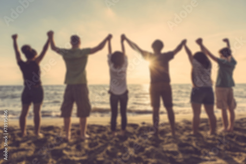 Group of people with raised arms at seaside, blurred background