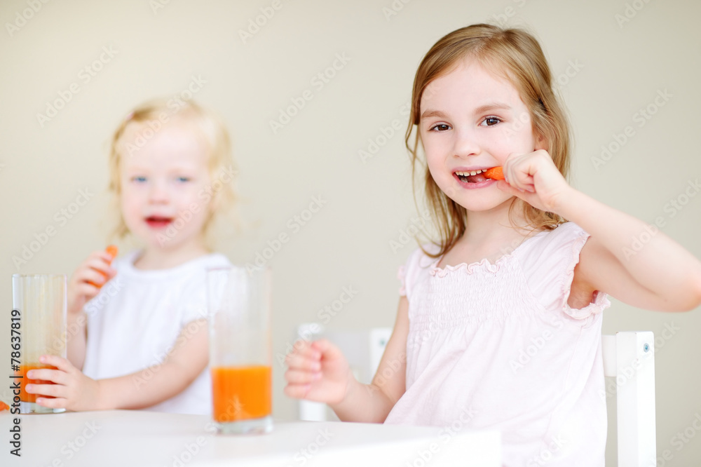 Two cute little sisters drinking carrot juice Two cute little sisters drinking carrot juice