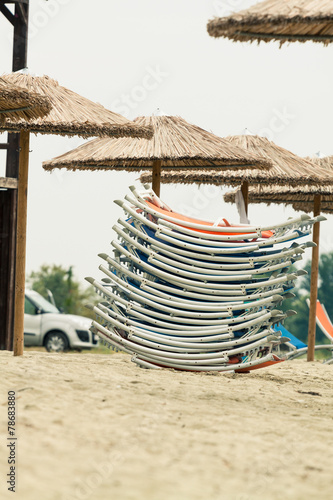 Straw umbrellas and a pack of sunbeds at a beach. Photo with unt photo