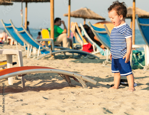 Toddler dressed as a sailor standing on a beach and crying with photo