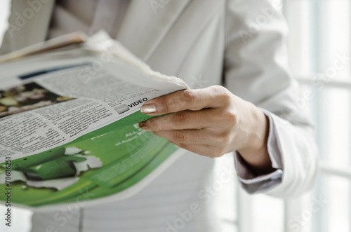 Businesswoman reading newspaper in front of window