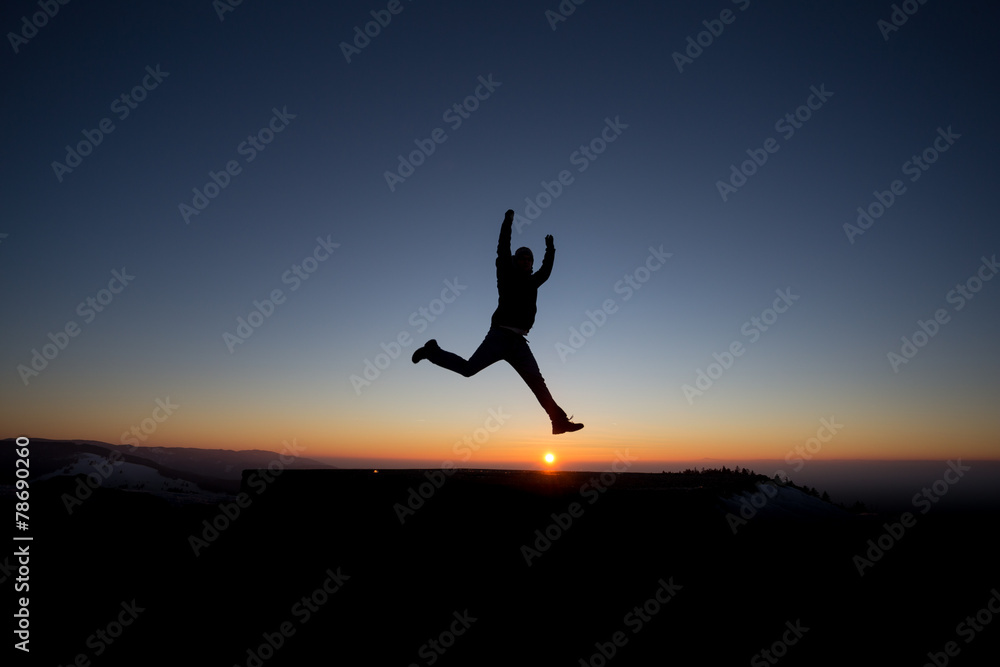 silhouetted man jumping on mountain in sunset