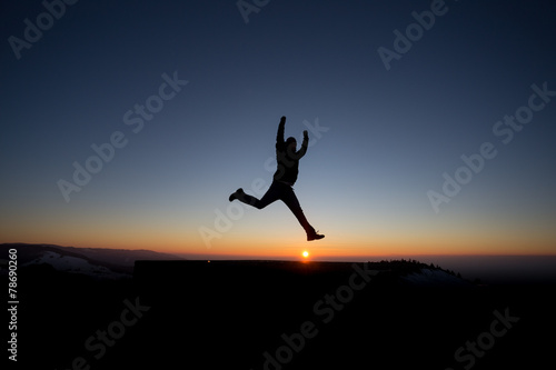 silhouetted man jumping on mountain in sunset