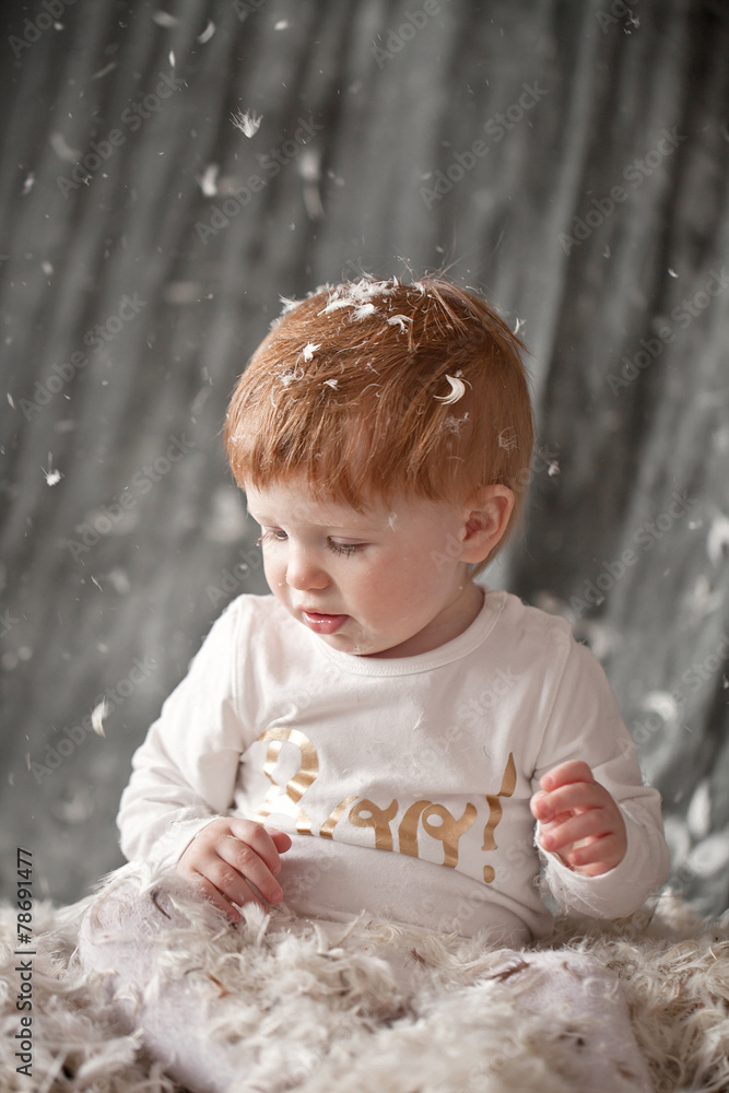 Baby Newborn with feather. Child Sitting at feathers pile and ca Baby Newborn with feather. Child Sitting at feathers pile and ca