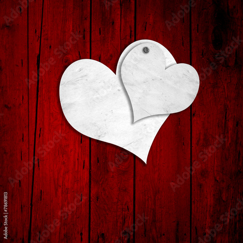 Conceptual two white old paper vintage hearts on red wood