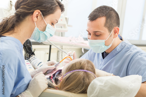 Dentist and dental assistant examining young girl teeth