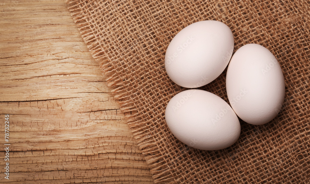 White eggs on burlap over wooden background White eggs on burlap over wooden background
