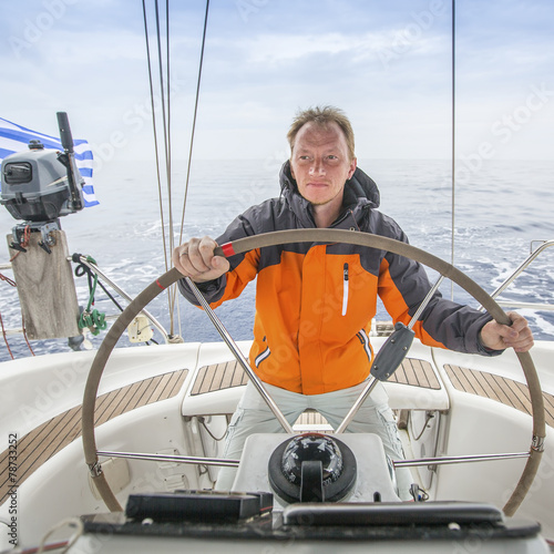 Young man Skipper at the helm of a yacht in the open sea.