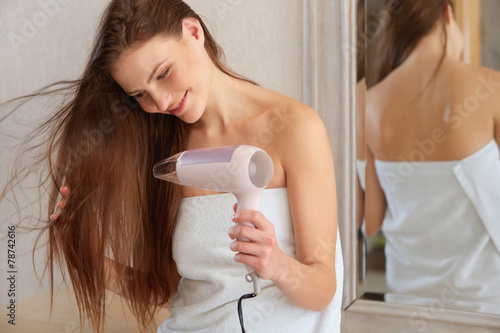 Foto Hair. Young woman blow drying hair in bathroom