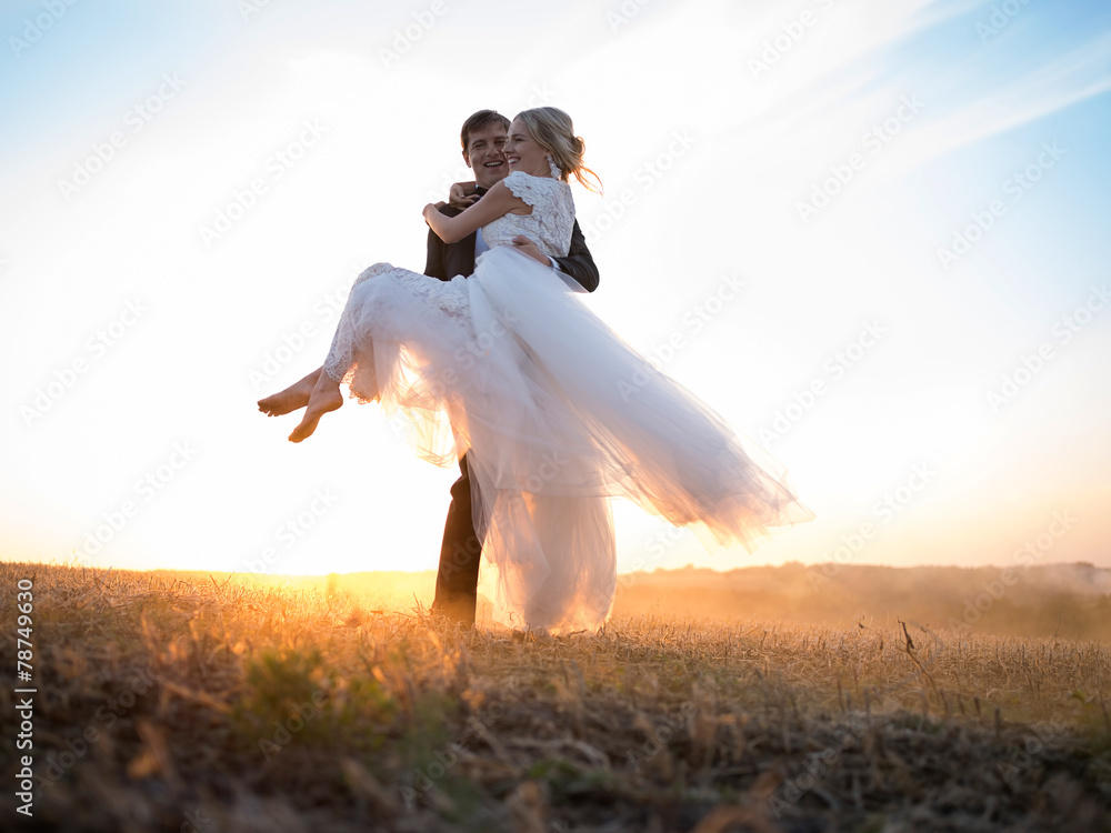 Husband carries his beloved wife in his arms, in the setting sun Husband carries his beloved wife in his arms, in the setting sun