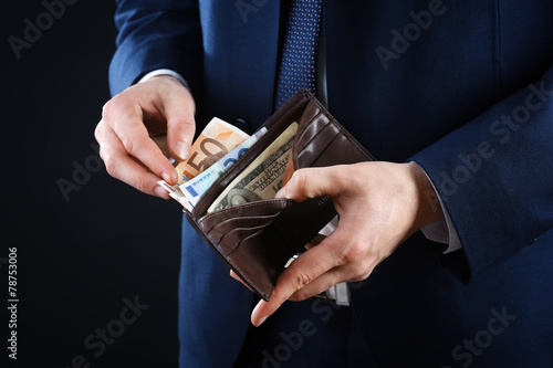 Leather wallet with money in male hands on dark background