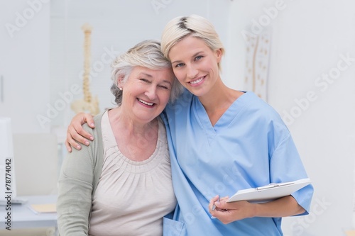 Friendly nurse with arm around senior patient in clinic