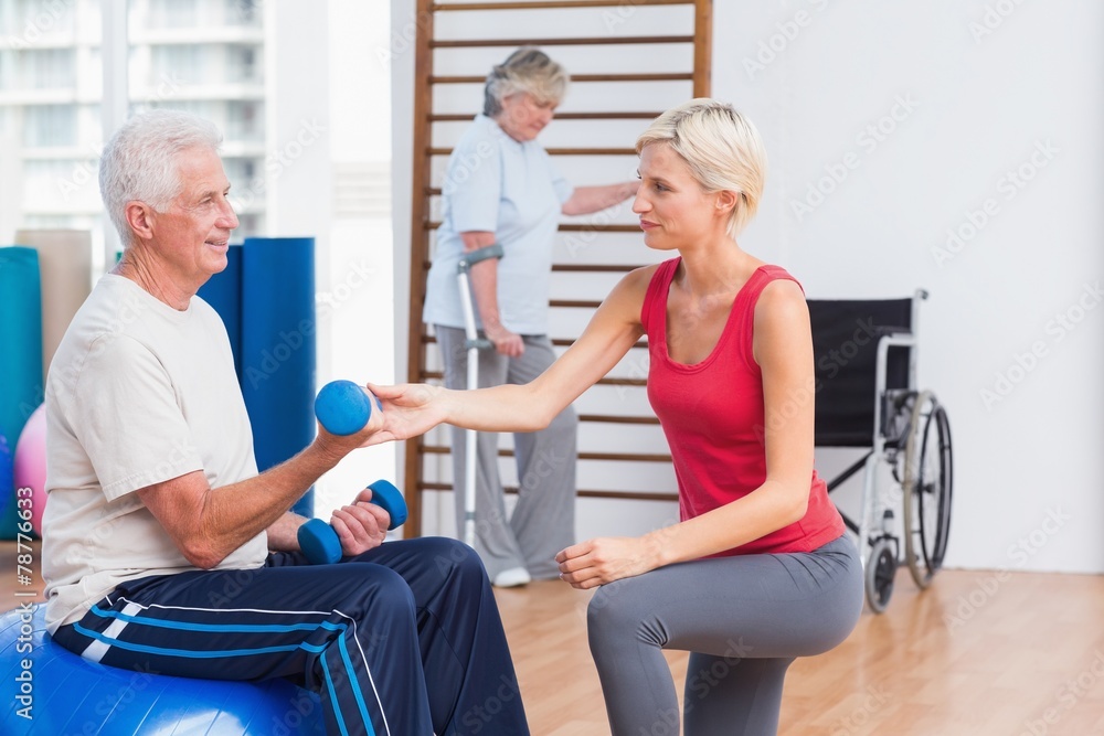 Trainer assisting senior man in exercising with dumbbells Trainer assisting senior man in exercising with dumbbells