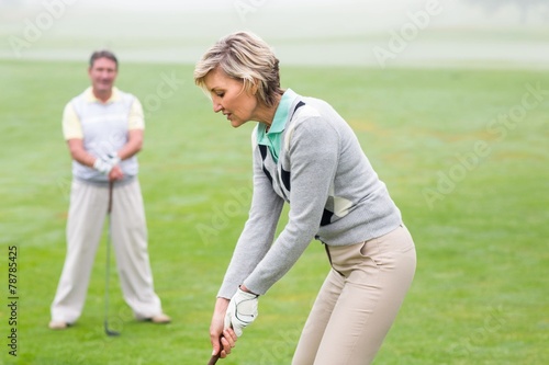 Lady golfer teeing off for the day watched by partner