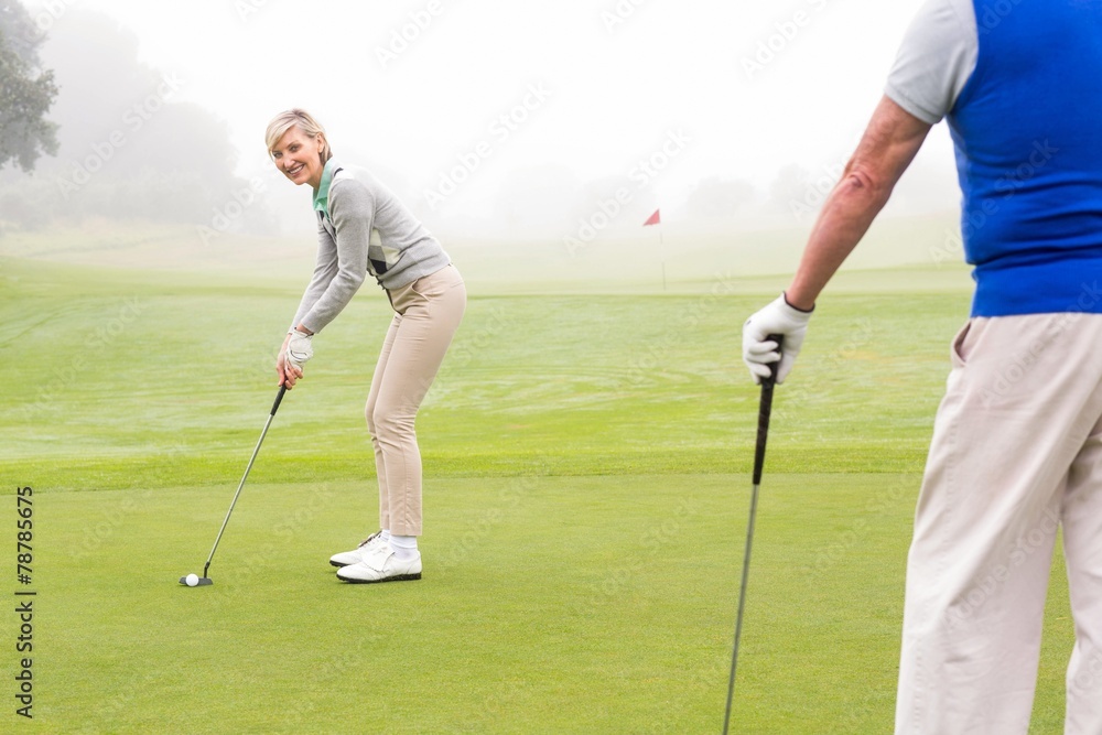 Fototapeta premium Lady golfer teeing off for the day watched by partner