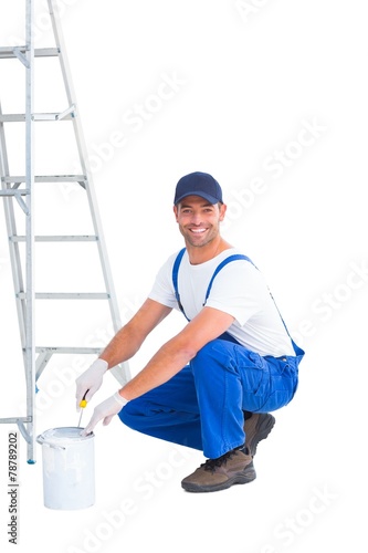 Smiling handyman in overalls opening paint can